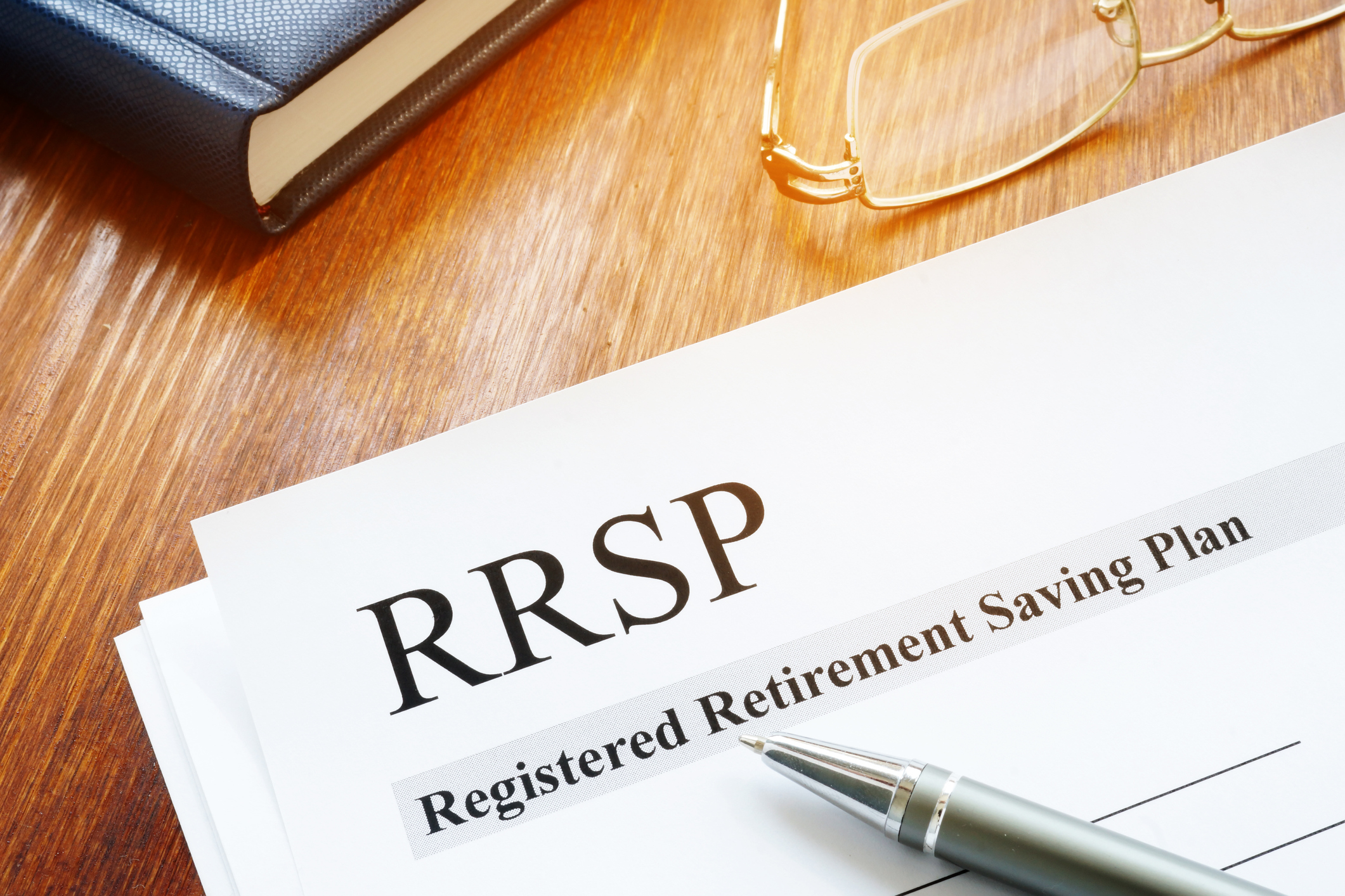 A close-up of a document labelled “RRSP: Registered Retirement Saving Plan” that sits on a desk near a notebook and a pair of glasses with a silver pen laying on top.