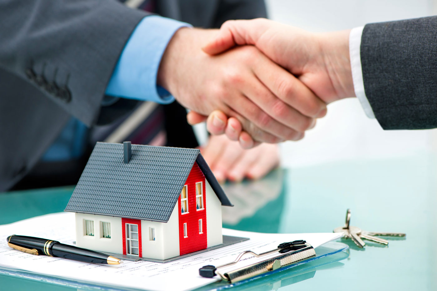 Two individuals handshaking over mortgage paperwork with a miniature house and keys, symbolizing a deal with a mortgage broker.